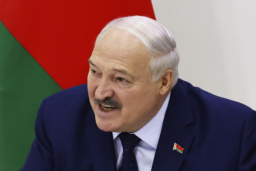 Крупный план Александра Лукашенко во время официального выступления. На пиджаке — значок с флагом Беларуси, на заднем плане — красно-зеленый фон.