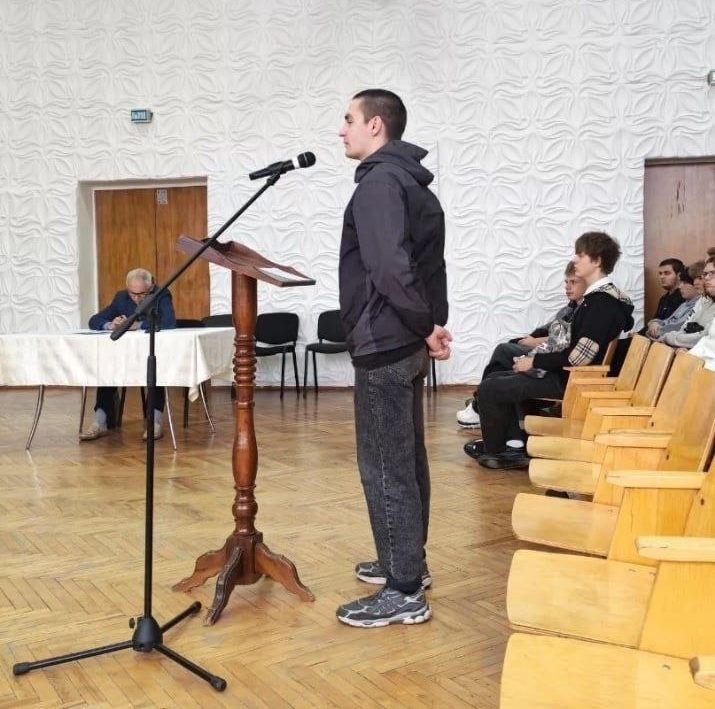 парень в актовом зале говорит в микрофон